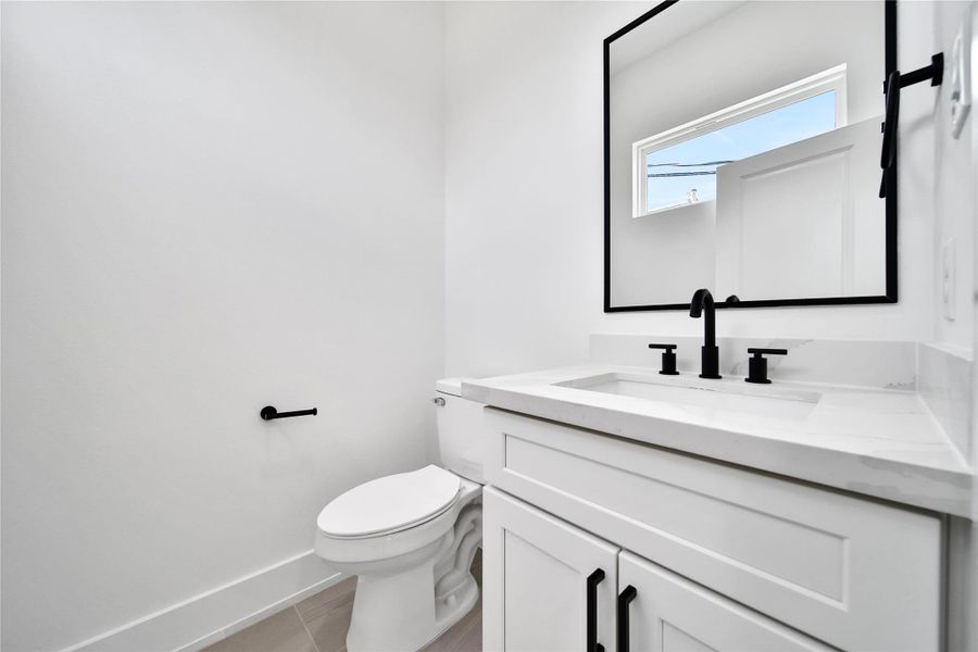 This is a modern, minimalist podwer bathroom featuring a white vanity with black fixtures, a square mirror, and a bright window for natural light.