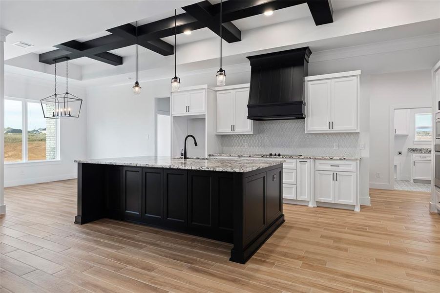 Kitchen featuring light wood-type flooring, custom range hood, coffered ceiling, tasteful backsplash, and beam ceiling