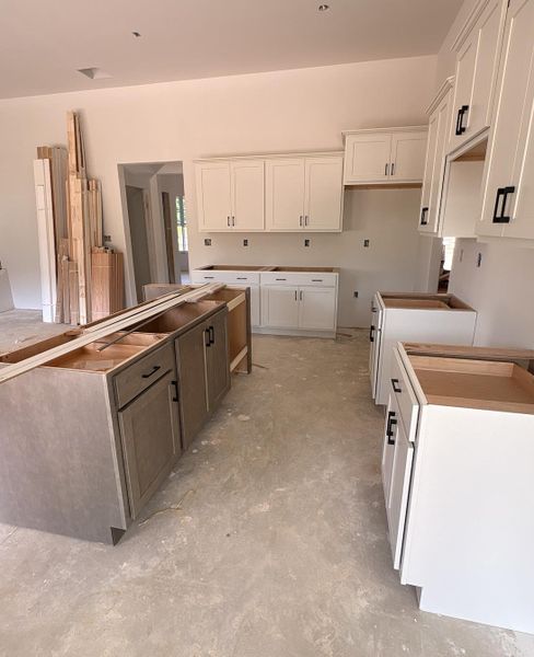 Kitchen featuring white upper and base cabinetry, a central island with wood-finish cabinetry, and matte black hardware