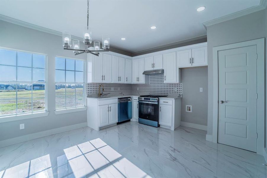 Kitchen with crown molding, stainless steel appliances, white cabinetry, decorative light fixtures, and light countertops