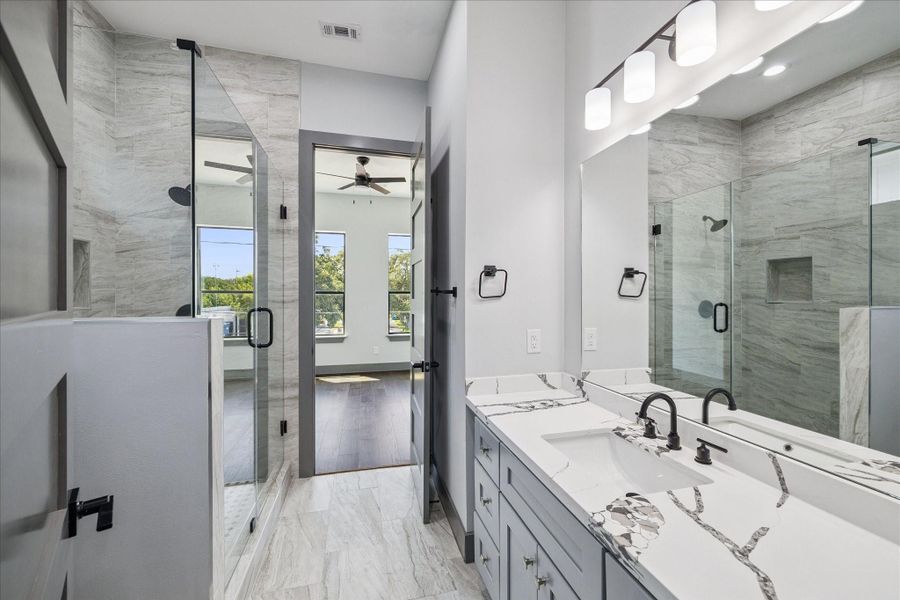 Connected to the secondary bedroom, this ensuite bathroom features a spacious walk-in shower with modern tile surround, a dual vanity with quartz counters, and matte black fixtures. The layout offers both function and style, making it a practical and comfortable space for everyday use.