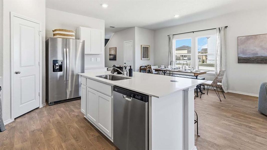Open-concept kitchen featuring an island with integrated sink, white cabinetry, stainless steel appliances, and wood-finish flooring
