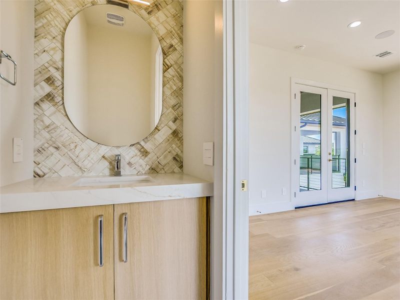 Modern vanity with a natural stone countertop, a vessel sink, and a unique tile backsplash