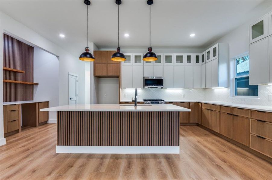 Kitchen with brown cabinets, a center island with sink, light wood finished floors, glass insert cabinets, and recessed lighting