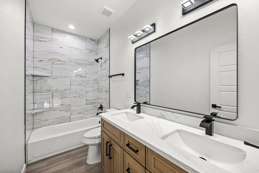 Elegant bathroom featuring a double vanity with a sleek quartz countertop, modern fixtures, and a spacious tub with a stylish tile surround.