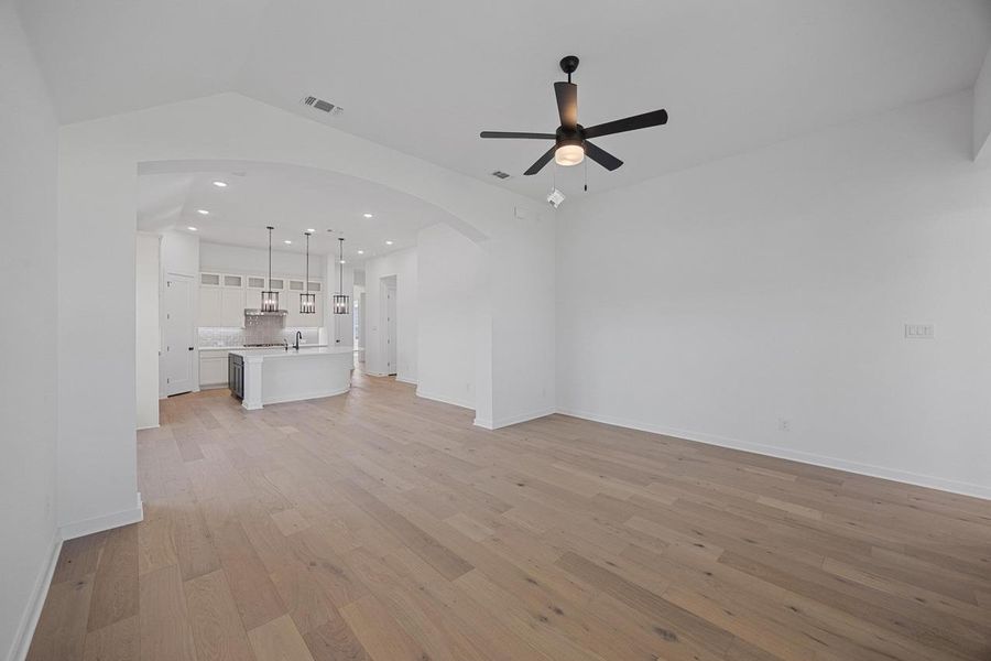 Unfurnished living room featuring arched walkways, ceiling fan, light wood-style floors, recessed lighting, and lofted ceiling