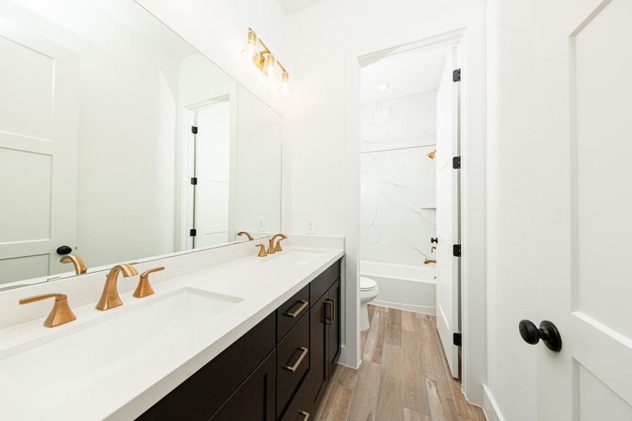 This secondary bathroom features a modern vanity with dual vanity sinks, tub/shower combination with gorgeous tile surround, and modern brushed gold finishes.
