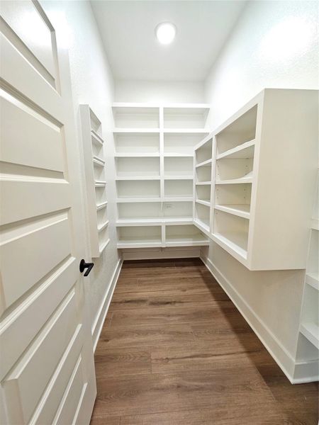 This photo showcases a spacious walk-in pantry with ample white shelving for storage, wood flooring, and bright lighting, ideal for organizing kitchen essentials. This photo showcases a spacious walk-in pantry with ample white shelving for storage, wood flooring, and bright lighting, ideal for organizing kitchen essentials.