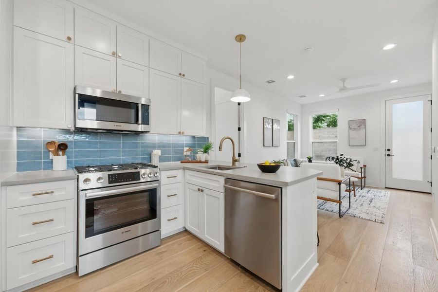 Kitchen featuring stainless steel appliances, backsplash, white cabinetry, light wood-type flooring, and decorative light fixtures Kitchen featuring stainless steel appliances, backsplash, white cabinetry, light wood-type flooring, and decorative light fixtures