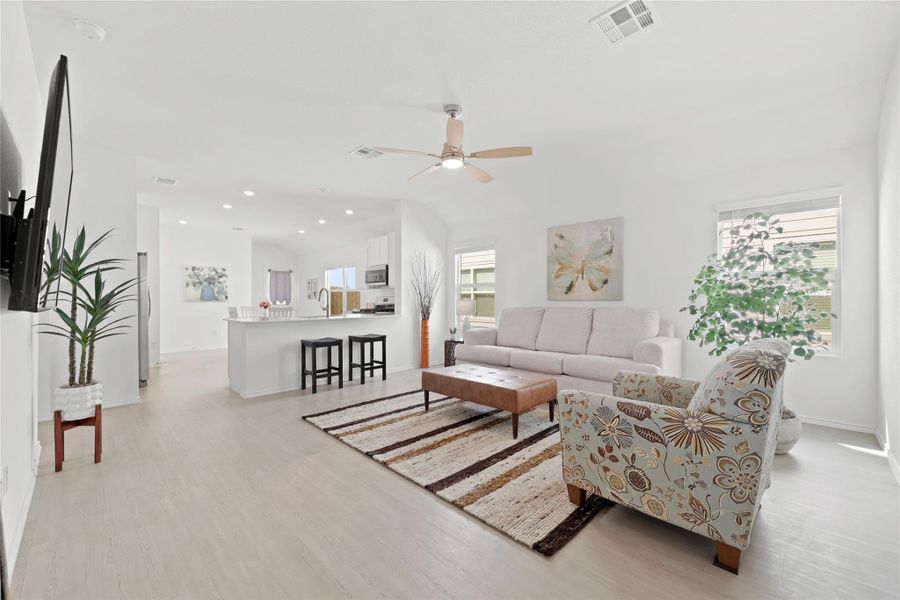 This sun-drenched, open-concept floor plan seamlessly connects the living area to a gourmet kitchen, enhanced by vaulted ceilings, recessed lighting, and durable wood-look flooring.