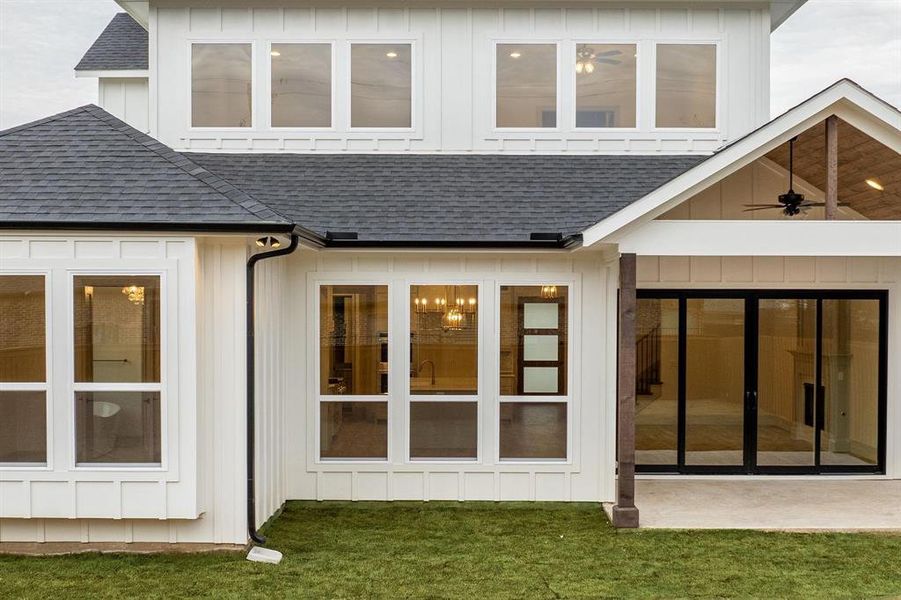 Rear view of property featuring roof with shingles, a ceiling fan, a lawn, and board and batten siding
