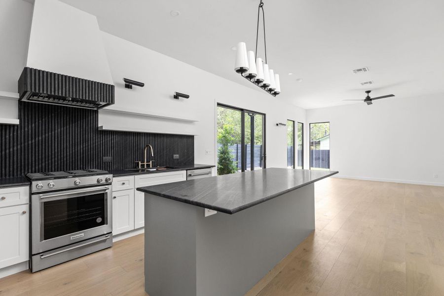 Kitchen with stainless steel appliances, dark countertops, white cabinets, a center island, and light wood-style floors