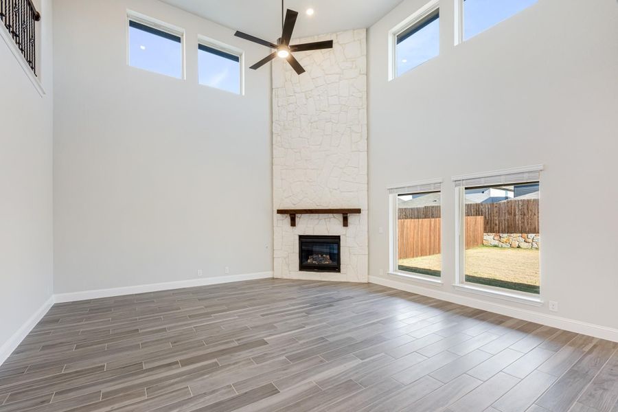 Open living room with two-story ceiling, floor-to-ceiling stone fireplace, ceiling fan, and wood-look tile floors Open living room with two-story ceiling, floor-to-ceiling stone fireplace, ceiling fan, and wood-look tile floors