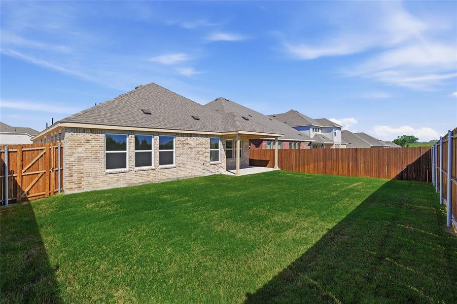 Expansive backyard featuring a manicured lawn, a covered patio, new wood fencing, and a brick exterior