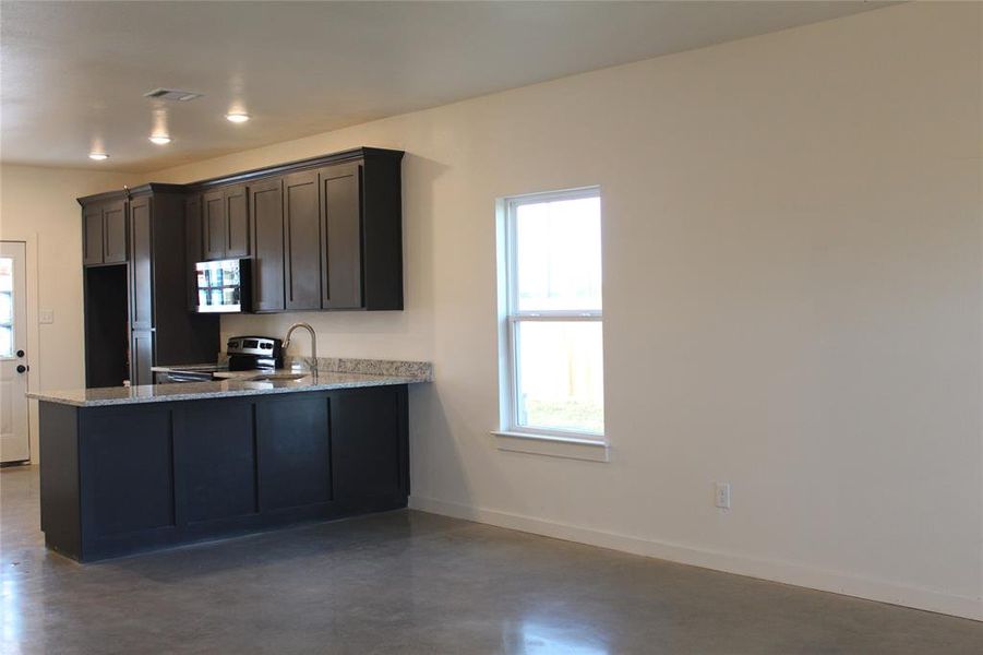 Kitchen with light stone counters, sink, kitchen peninsula, concrete flooring, and appliances with stainless steel finishes