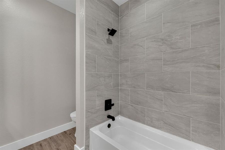 Bathroom with tiled shower / bath combo, toilet, and wood-type flooring