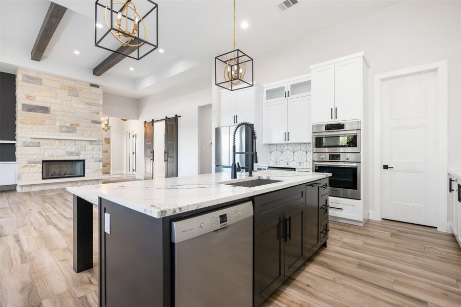 Kitchen with decorative light fixtures, white cabinetry, stainless steel appliances, a kitchen island with sink, and a barn door