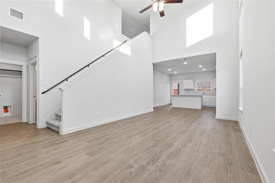 Open-concept living area featuring wood-finish flooring, a two-story ceiling, and a modern ceiling fan Open-concept living area featuring wood-finish flooring, a two-story ceiling, and a modern ceiling fan