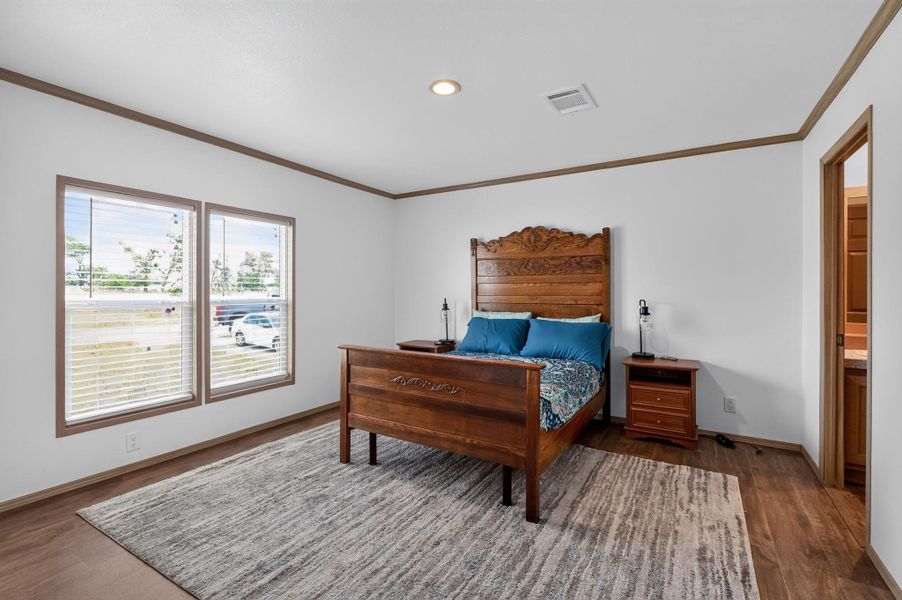 Hardwood-style flooring and crown molding define this well-lit bedroom space.