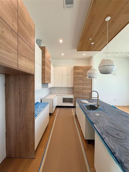 Kitchen featuring modern cabinets, pendant lighting, light wood-style floors, dark stone countertops, and recessed lighting