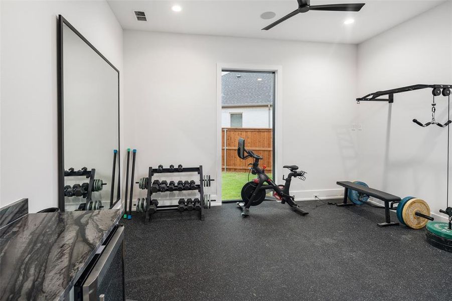 Dedicated home gym designed for convenient at-home workouts, featuring durable flooring and space for multiple fitness stations. Built-in shelving and a beverage fridge add functionality and convenience, creating a well-equipped space for both training and recovery.