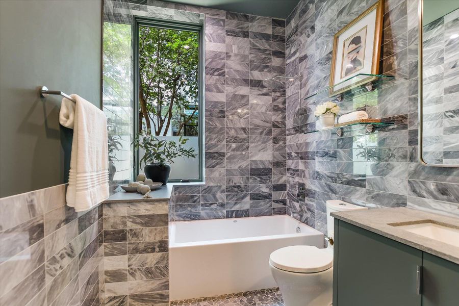 Bathroom featuring a built-in bathtub, a window with frosted lower glass, and grey marble-look subway tile walls