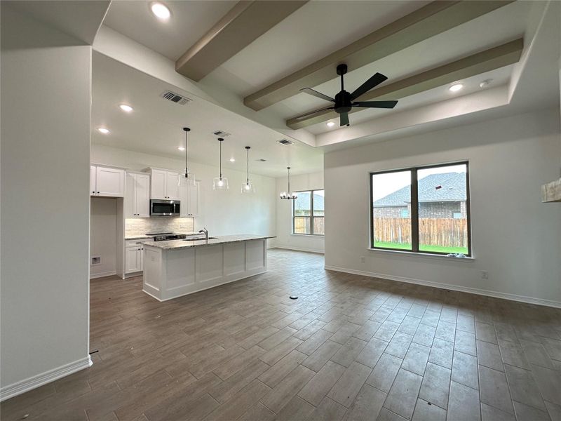 Expansive open-concept living space featuring wood-finish tile flooring, a tray ceiling with decorative beams, and a black ceiling fan