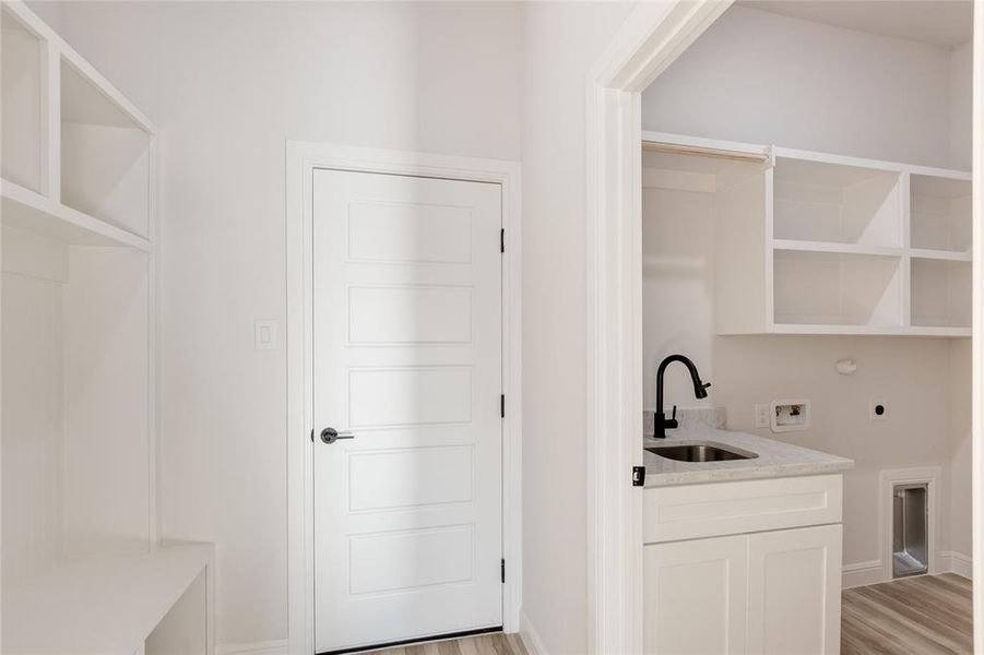 Entrance from the garage to a mud room and laundry room with washer hookup, gas dryer hookup, hookup for an electric dryer, and light wood-style floors.