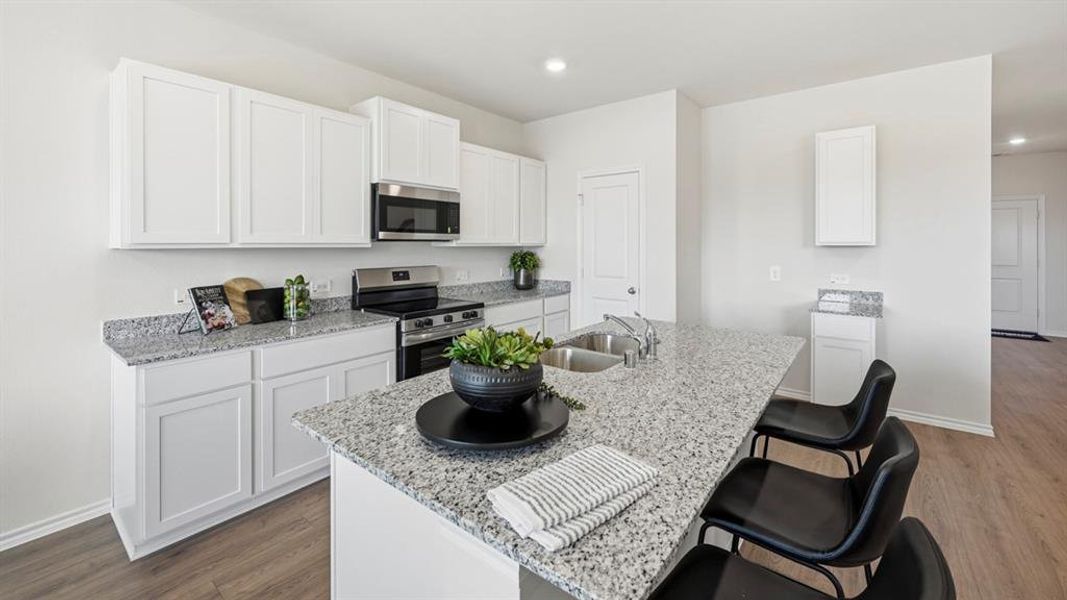 Kitchen featuring light stone counters, stainless steel appliances, white cabinetry, a kitchen bar, and recessed lighting Kitchen featuring light stone counters, stainless steel appliances, white cabinetry, a kitchen bar, and recessed lighting