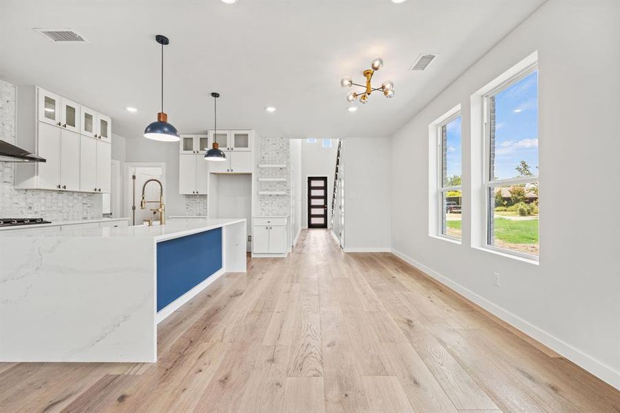 Kitchen with decorative light fixtures, decorative backsplash, light wood-type flooring, light stone countertops, and white cabinetry