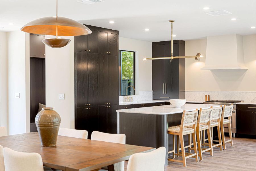 Kitchen with light stone countertops, stainless steel range with gas cooktop, a breakfast bar area, hanging light fixtures, and a kitchen island