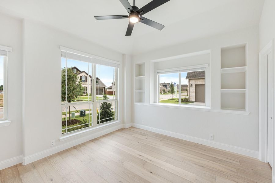 Empty room with light wood floors, ceiling fan, large windows, and built-in wall shelves Empty room with light wood floors, ceiling fan, large windows, and built-in wall shelves
