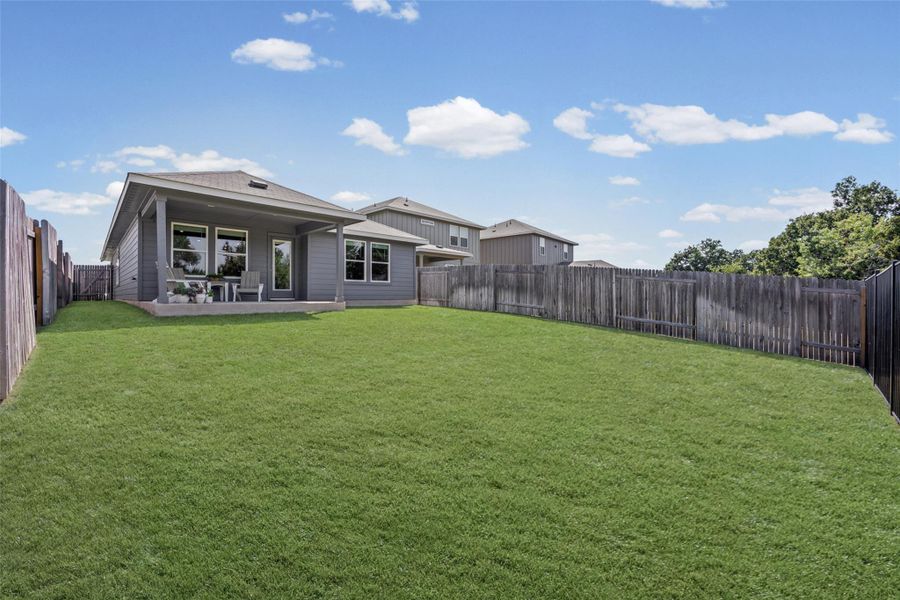 An expansive green lawn stretches across a fully fenced backyard with a covered patio.
