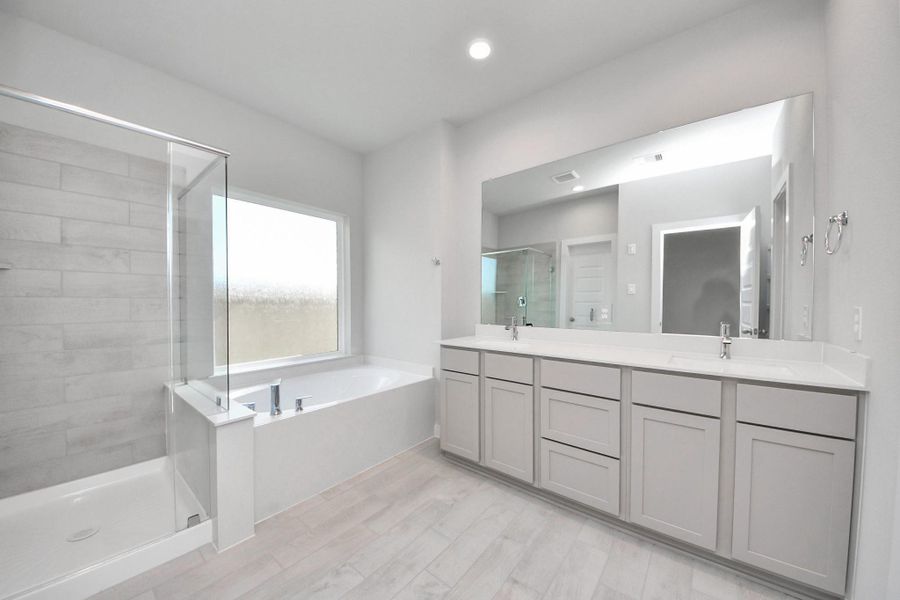 Escape to a spa-like oasis in this primary bathroom. Enjoy a walk-in shower with tile surround, a separate garden tub with custom detailing, and an elegant vanity featuring light countertops, modern hardware, and beautiful vanity lights. Experience luxury and relaxation in every detail. Sample photo of completed home with similar floor plan. Actual colors and selections may vary. Escape to a spa-like oasis in this primary bathroom. Enjoy a walk-in shower with tile surround, a separate garden tub with custom detailing, and an elegant vanity featuring light countertops, modern hardware, and beautiful vanity lights. Experience luxury and relaxation in every detail. Sample photo of completed home with similar floor plan. Actual colors and selections may vary.