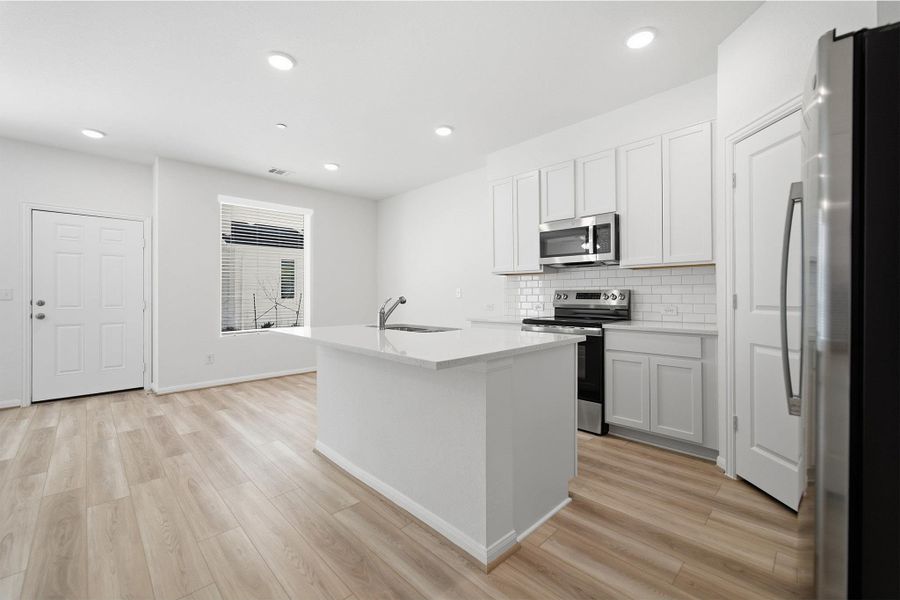 Kitchen featuring stainless steel appliances, a kitchen island with sink, light wood finished floors, white cabinetry, and decorative backsplash Kitchen featuring stainless steel appliances, a kitchen island with sink, light wood finished floors, white cabinetry, and decorative backsplash