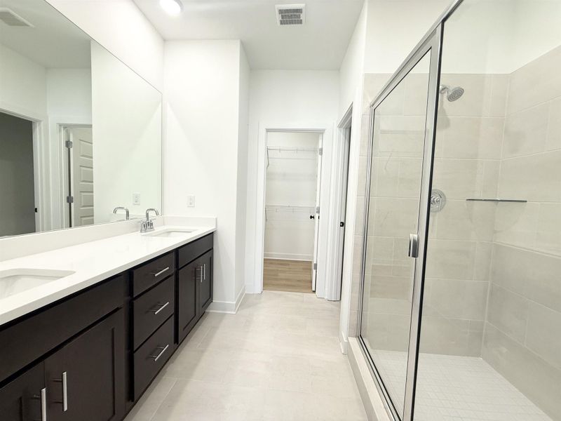 Full bathroom featuring double vanity, a shower stall, a spacious closet, and light tile patterned floors