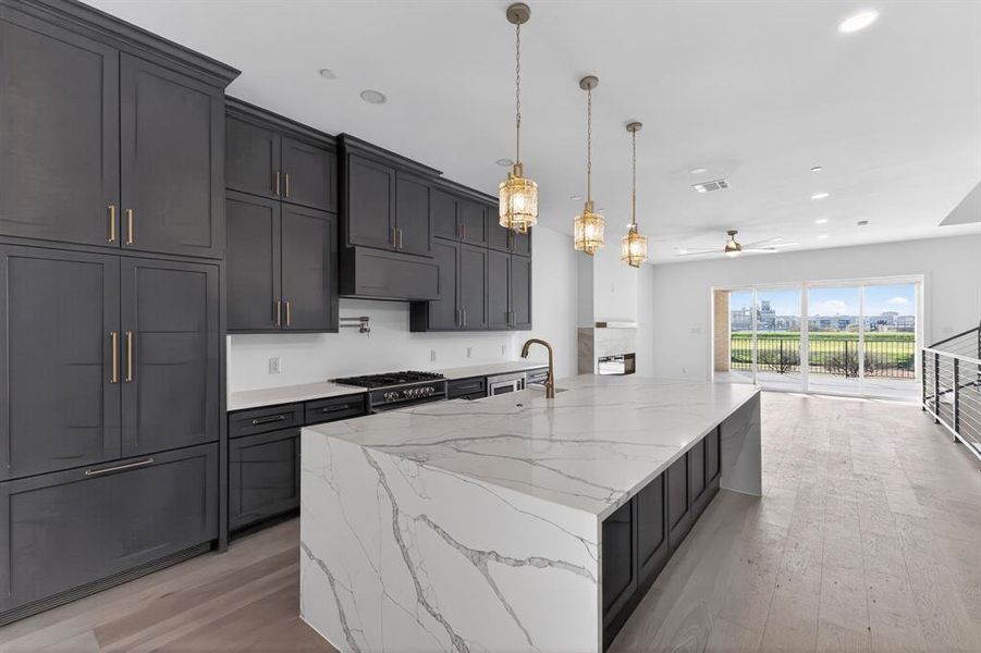 Kitchen featuring light stone countertops, light wood-style flooring, a large island, and dark cabinetry
