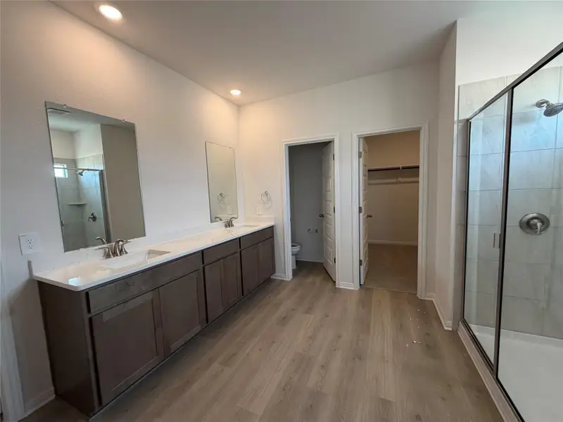 Full bath with a walk in closet, a stall shower, double vanity, light wood-style flooring, and recessed lighting
