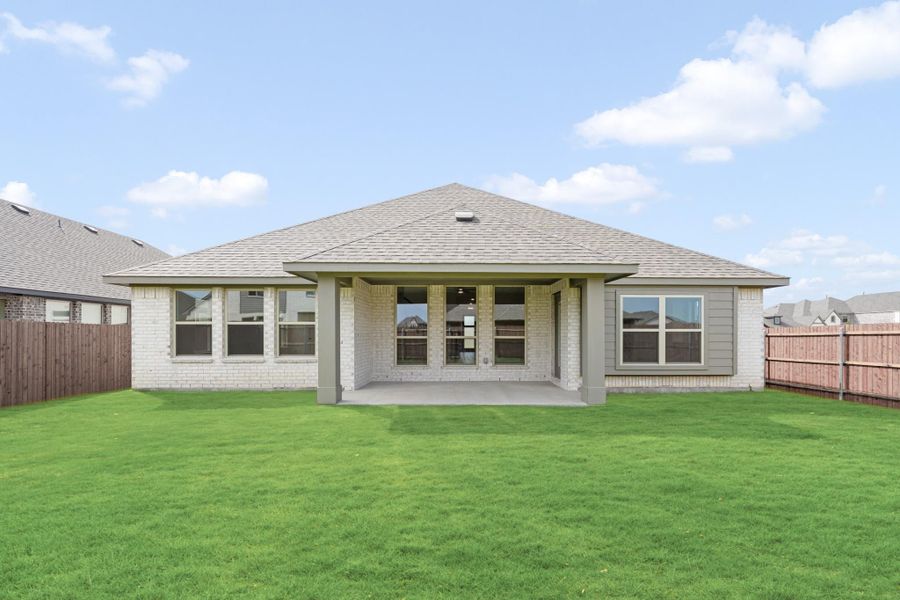Rear exterior of single-story brick home with covered patio, large windows, and fenced backyard with green lawn.