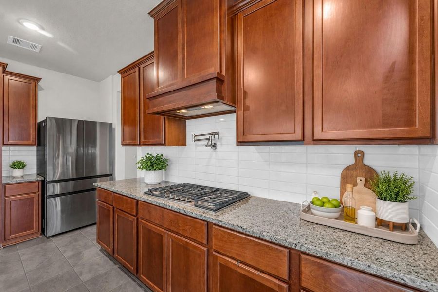 The gourmet cooking area showcases premium granite countertops, a classic white subway tile backsplash, a built-in gas cooktop, and a convenient pot filler faucet. The gourmet cooking area showcases premium granite countertops, a classic white subway tile backsplash, a built-in gas cooktop, and a convenient pot filler faucet.