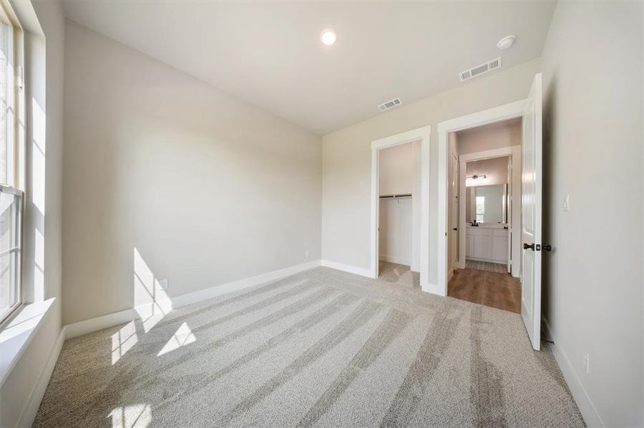 Unfurnished bedroom with light carpet, multiple windows, and a walk in closet Unfurnished bedroom with light carpet, multiple windows, and a walk in closet