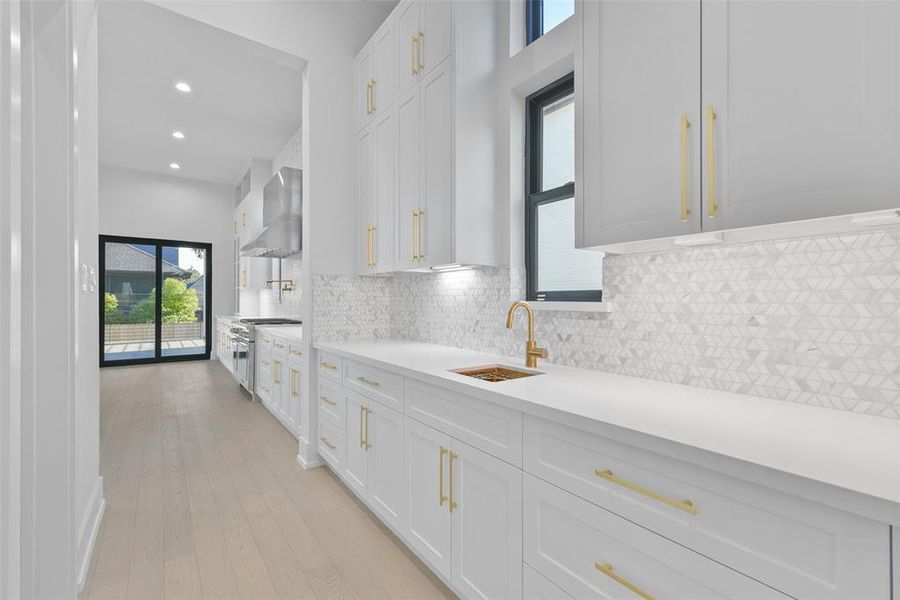 The Butler's Pantry with an additional sink and great countertop space flows seamlessly through to the kitchen and formal dining spaces making entertaining fun and easy. The quartzite countertops and marble backsplash are complemented by the brass finishes.