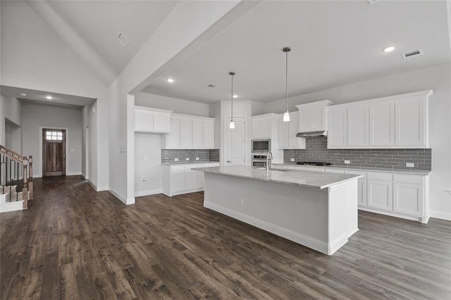 Kitchen featuring appliances with stainless steel finishes, a center island with sink, dark wood finished floors, visible vents, and white cabinets