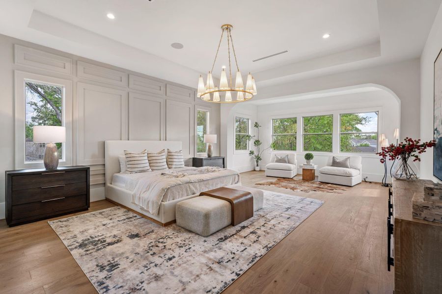 The primary suite offers an expansive retreat with high ceilings, detailed wall paneling, and multiple windows that fill the room with natural light. A separate sitting area adds flexibility and comfort.