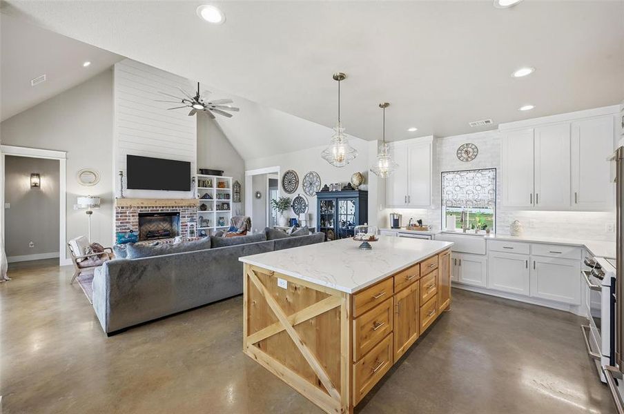Kitchen featuring white cabinetry, a brick fireplace, concrete floors, decorative backsplash, and high vaulted ceiling Kitchen featuring white cabinetry, a brick fireplace, concrete floors, decorative backsplash, and high vaulted ceiling