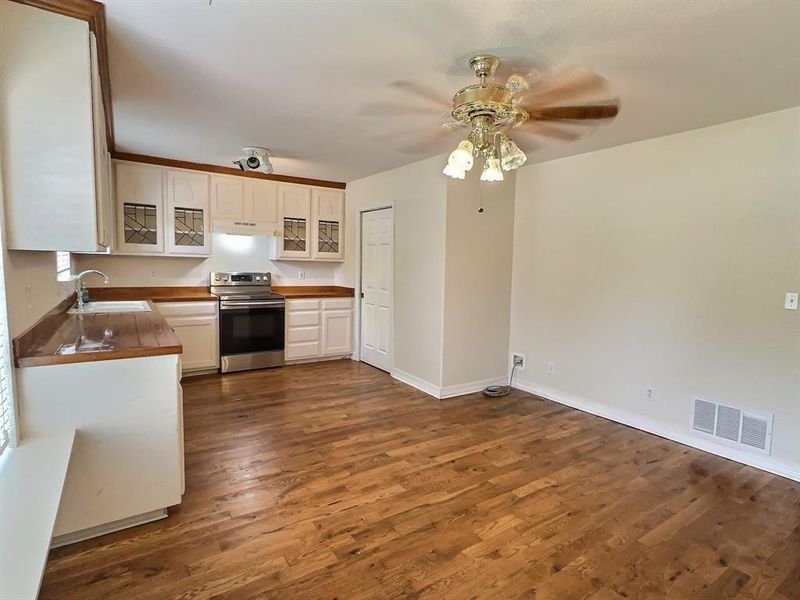 Kitchen featuring stainless steel electric stove, white cabinetry, glass insert cabinets, a ceiling fan, and dark wood-style flooring