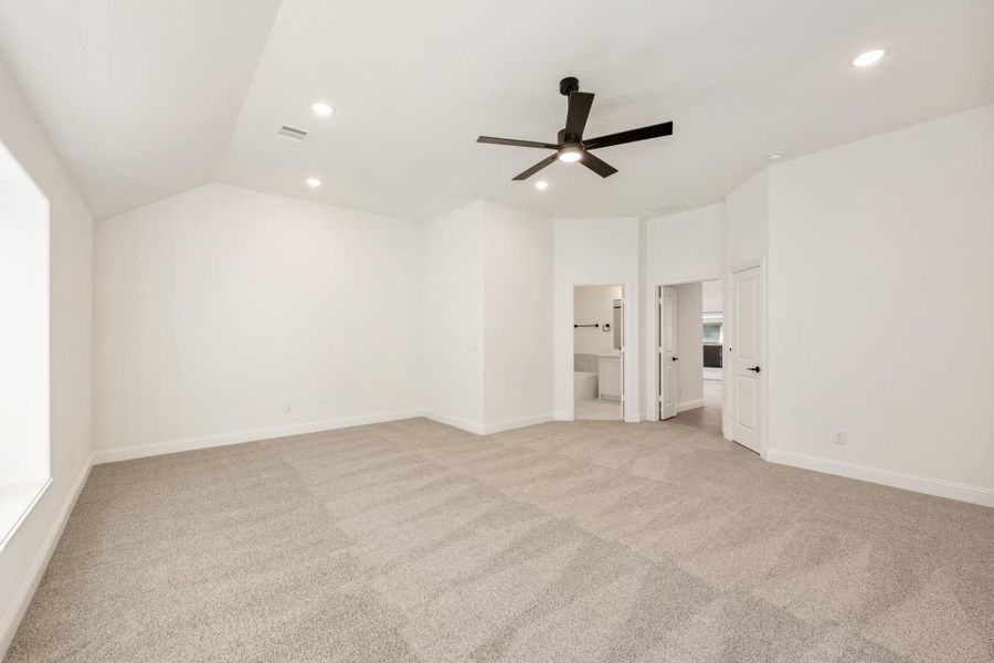 Spacious empty bedroom with vaulted ceiling, ceiling fan, carpet flooring, and doors leading to bathroom and closet