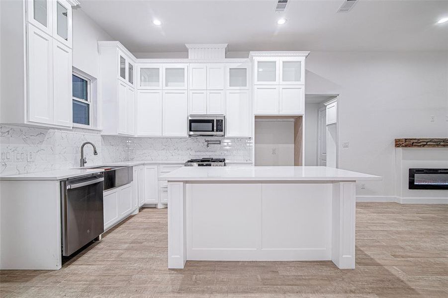 Kitchen featuring stainless steel appliances, a sink, a center island, backsplash, and light countertops Kitchen featuring stainless steel appliances, a sink, a center island, backsplash, and light countertops
