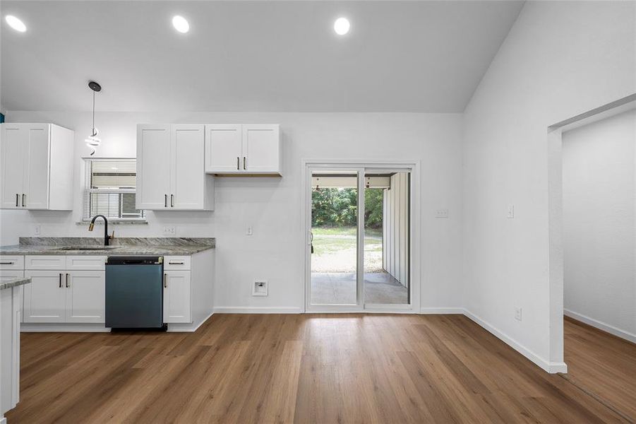 Kitchen featuring white cabinetry, stone countertops, a black appliance, wood-finish flooring, and sliding glass doors to the exterior Kitchen featuring white cabinetry, stone countertops, a black appliance, wood-finish flooring, and sliding glass doors to the exterior