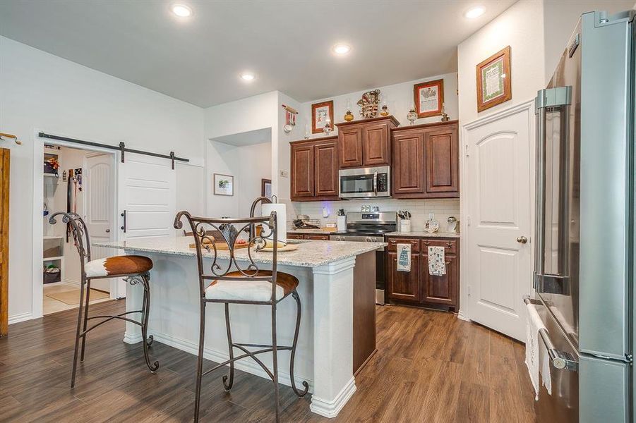 Kitchen featuring a barn door, appliances with stainless steel finishes, decorative backsplash, light stone countertops, and dark wood-style flooring Kitchen featuring a barn door, appliances with stainless steel finishes, decorative backsplash, light stone countertops, and dark wood-style flooring